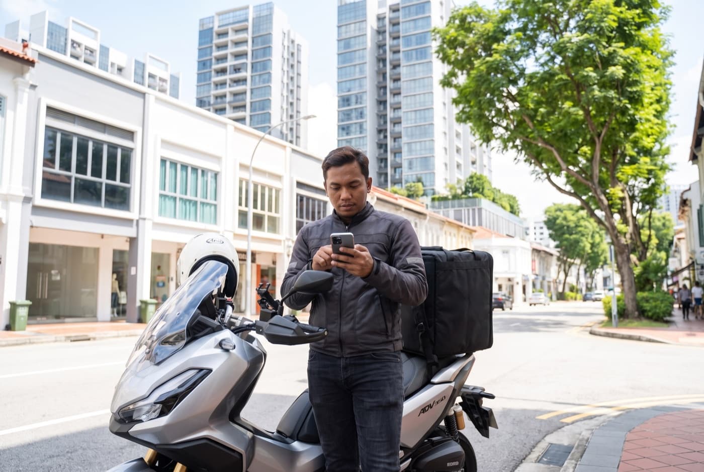 A rider browsing on his phone beside his bike on a Singapore shophouse street